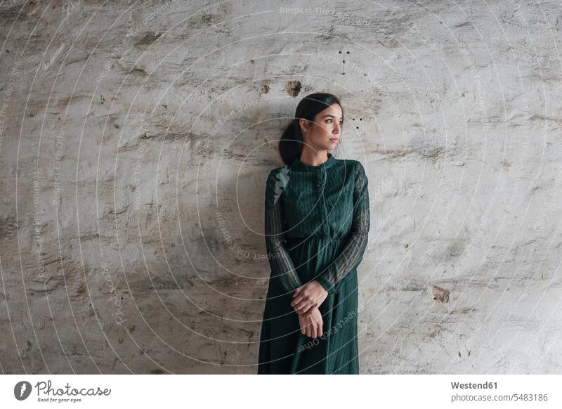 Young woman wearing green dress, staning in front of wall young serious earnest Seriousness austere dresses sad walls females women Emotion Feeling Feelings