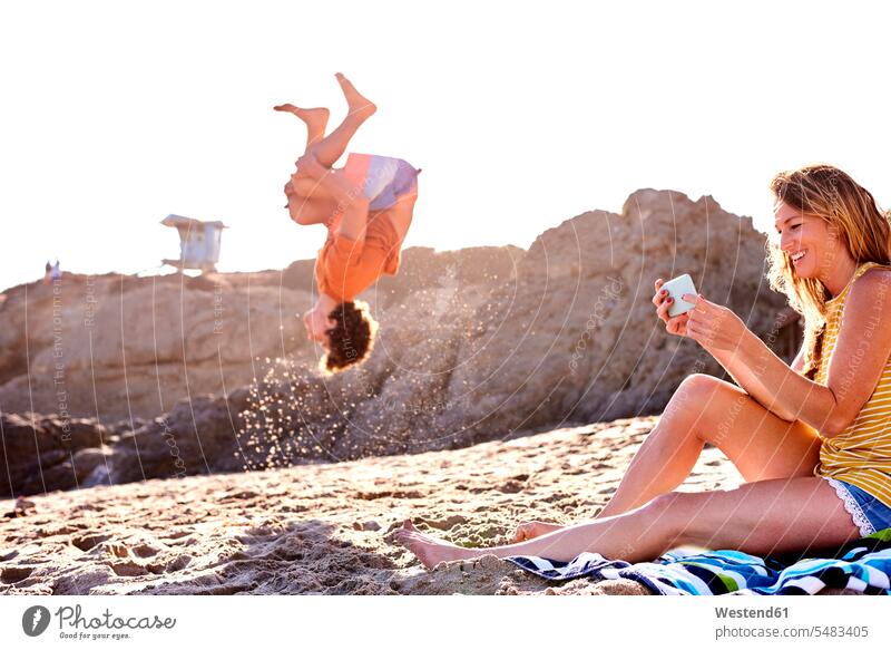 Young man on the beach doing a somersault with woman checking cell phone Somersaulting Flip somersaults mobile phone mobiles mobile phones Cellphone cell phones