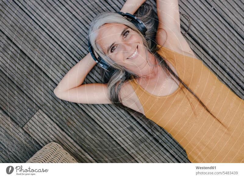 Portrait of happy woman lying on terrace listening music with headphones terraces portrait portraits laying down lie lying down females women hearing headset
