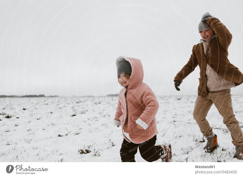 Brother and little sister playing together on snow-covered meadow brother brothers snow covered covered in snow snowy meadows sisters siblings