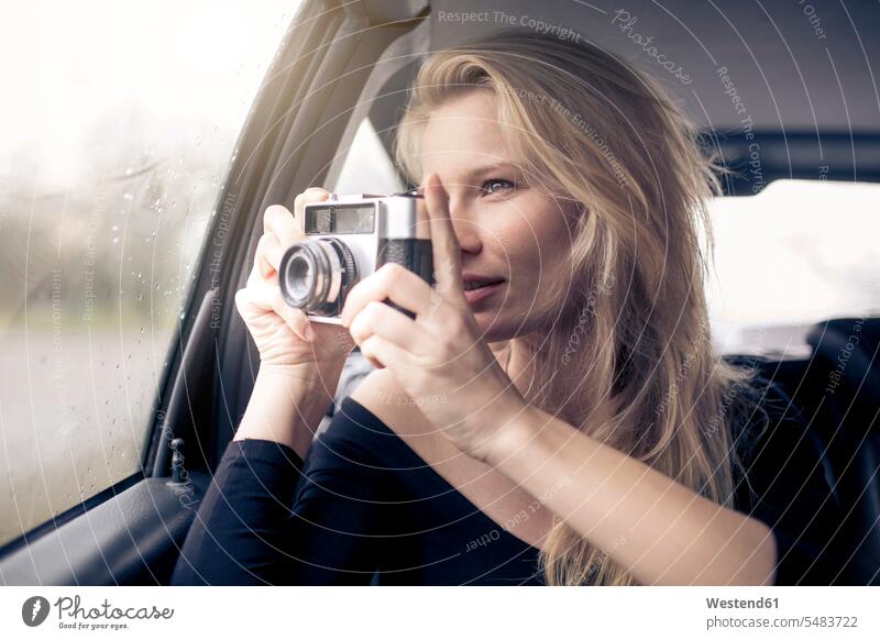 Woman sitting in car taking picture with camera automobile Auto cars motorcars Automobiles woman females women photographing portrait portraits motor vehicle