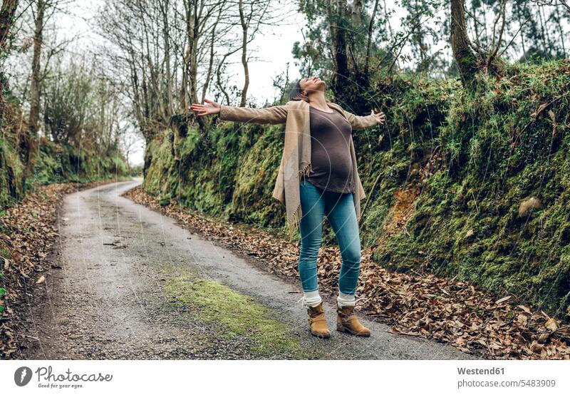 Happy pregnant woman raising her arms in forest in autumn females women Pregnant Woman Adults grown-ups grownups adult people persons human being humans