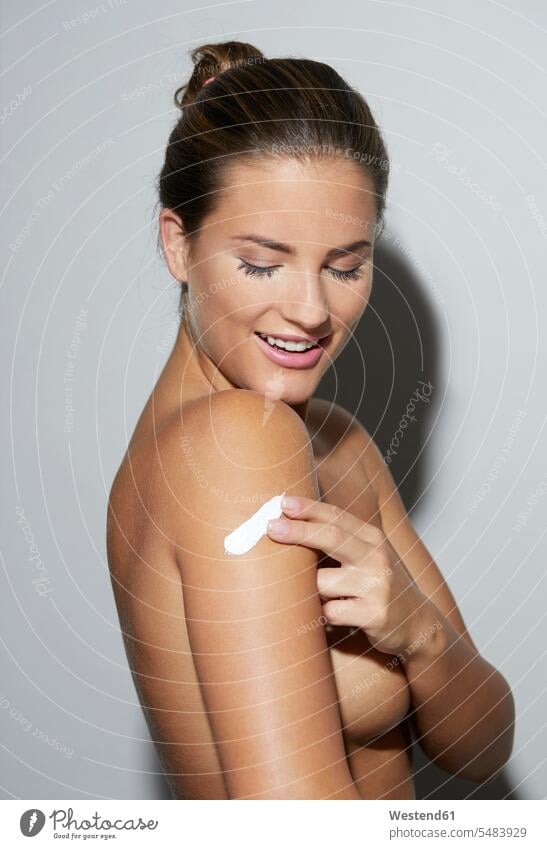Smiling beautiful young woman applying skin cream on her arm females women Beauty arms creaming smiling smile attractive pretty good-looking Attractiveness