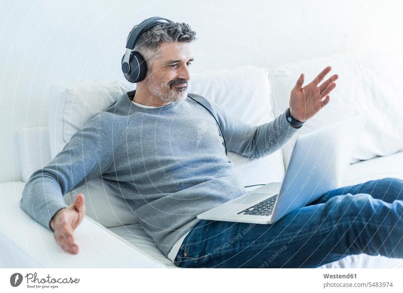 Mature man at home using laptop and wearing headphones hearing men males Laptop Computers laptops notebook headset couch settee sofa sofas couches settees