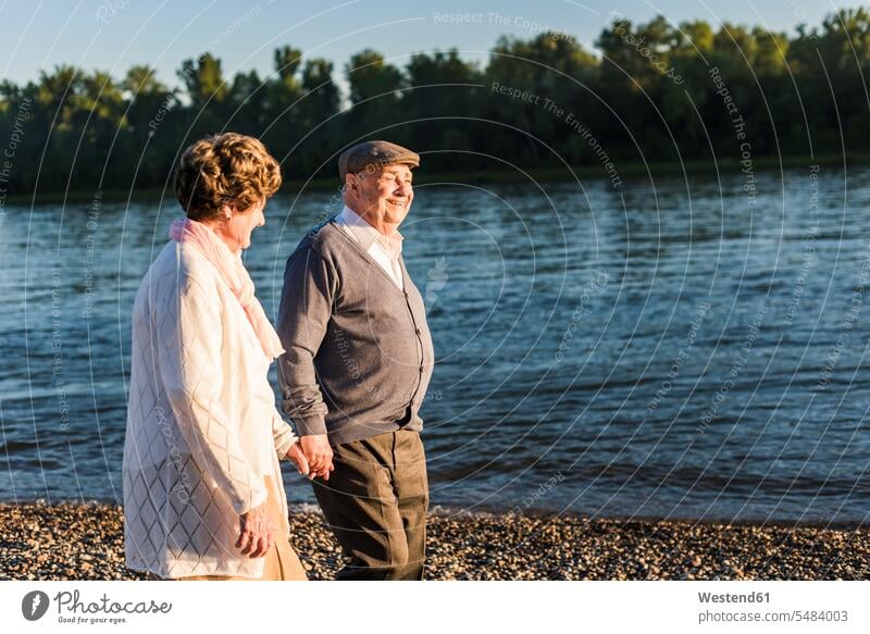 Happy senior couple walking hand in hand at riverside strolling taking a walk take a walk elder couples senior couples going adult couple adult couples twosomes