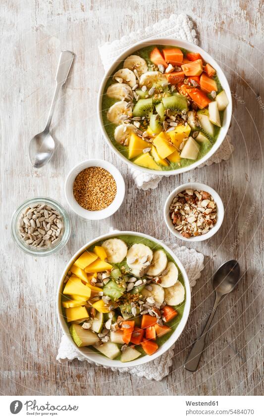 Smoothie bowl with different fruits, mango, papaya, kiwi, banana and pear and toppings, lineseeds, sunflower-seeds and nuts Series Part of A Series Spoon Spoons