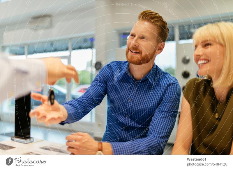 Salesperson handing over car keys to customers content pleased smiling smile seller sellers selling buying couple twosomes partnership couples automobile Auto