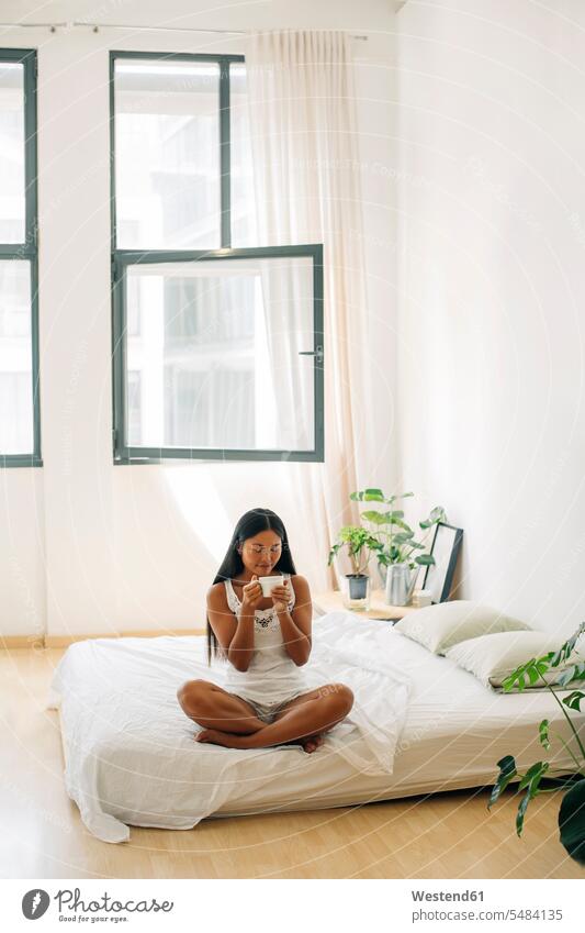 Young woman sitting on bed drinking coffee females women relaxed relaxation beds Coffee Adults grown-ups grownups adult people persons human being humans