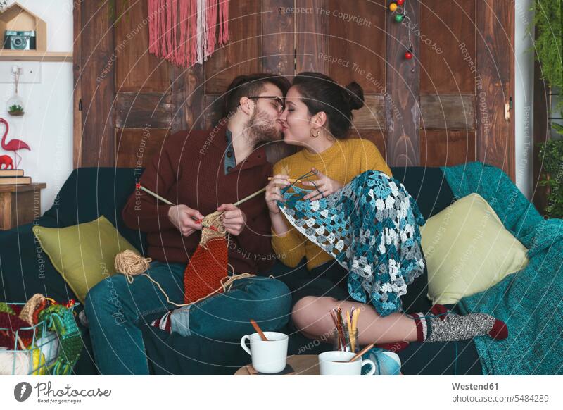 Young couple doing needleworks kissing on the couch twosomes partnership couples kisses people persons human being humans human beings sitting Seated hobby