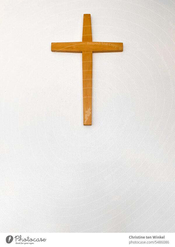 A simple wooden cross on a white wall Crucifix Christian cross Religion and faith Belief Christianity Spiritual guidance Sign Hope Symbols and metaphors