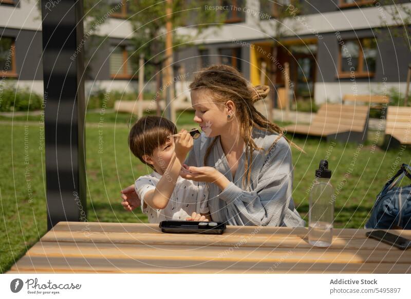 Boy feeding sushi to woman in park during summer mother son table boy family food share love dreadlocks lifestyle picnic little chopsticks sitting together