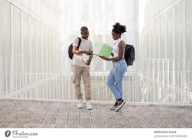 Black teenage lovers with book file on street couple student walk city relationship together backpack style contemporary lifestyle trendy modern black young