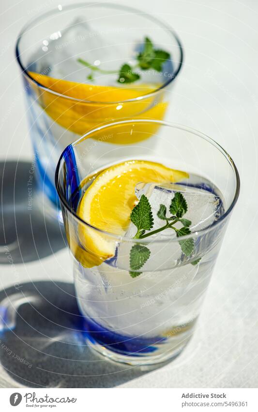 Summer cocktail with lemon vodka, slice of lemon and wild mint leaves summer leaf white table surface beverage glass transparent cube cool refreshment liquid