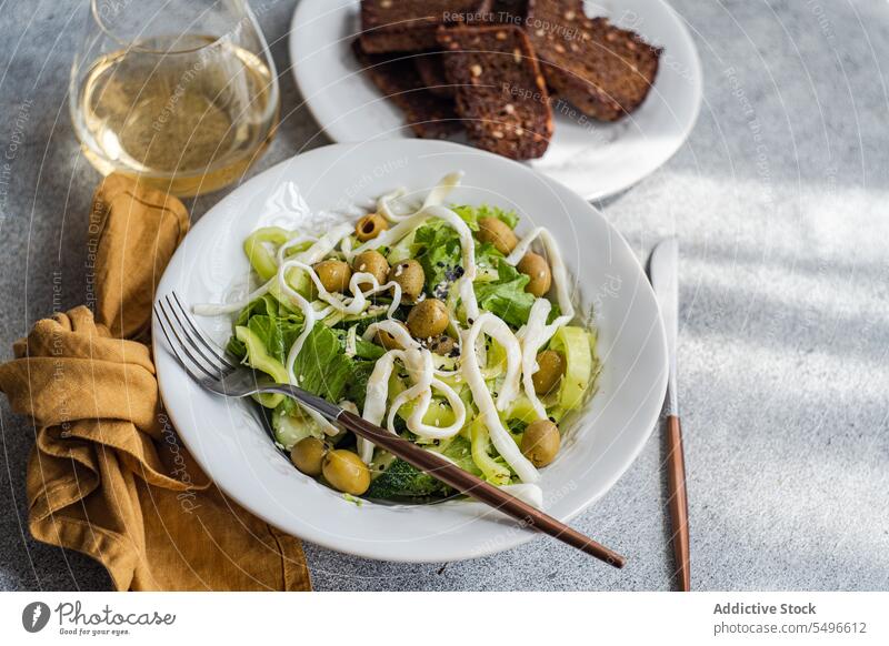 Vegetable salad with green vegetables like lettuce, cucumber, olives, green bell pepper with homemade cheese, sesame seeds plate dish bread wine glass wineglass