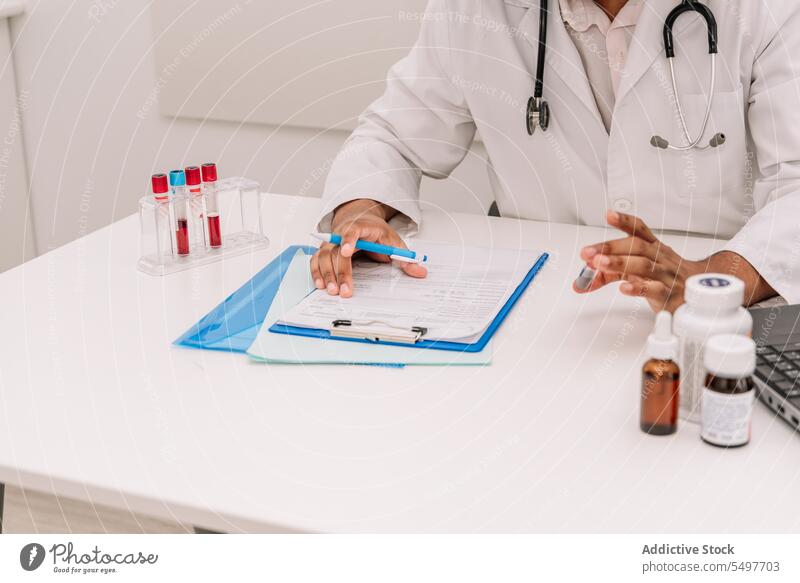 Focused doctor with blood test tube writing information in form after blood test man work write notes clipboard clinic hospital professional busy male job