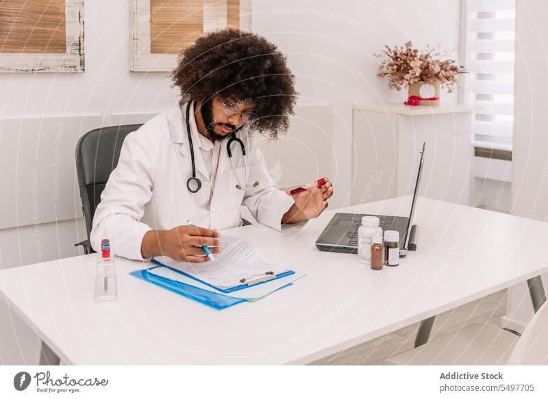 Focused doctor with blood test tube writing information in form after blood test man work write clipboard clinic take note hospital professional laptop busy