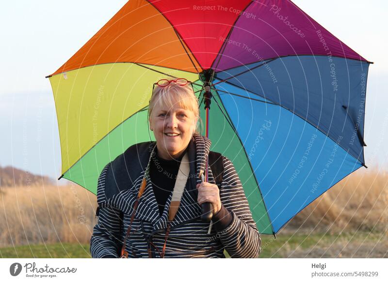 Portrait of friendly blonde middle aged woman holding colorful umbrella Human being Woman Friendliness Smiling kind Congenial portrait Adults Feminine