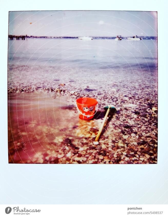 a sand bucket and a shovel in the water on the lakeshore. children's toys Polaroid Vacation & Travel Lake Lake Garda Lakeside Vacation photo Water Italy