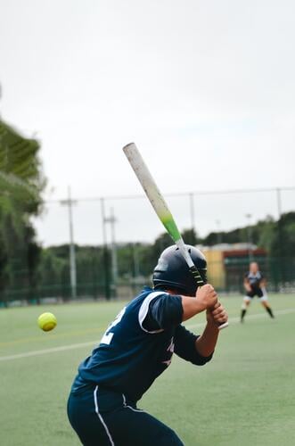 Softball player with back to camera has an approaching ball firmly fixed and takes a swing to hit it Baseball Lawn lawn sports Sports Ball Grass Playing