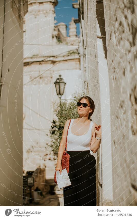 Female tourist with paper city map on narrow streets of Ostuni, Italy woman female tourist map direction navigation exterior tourism house building summer