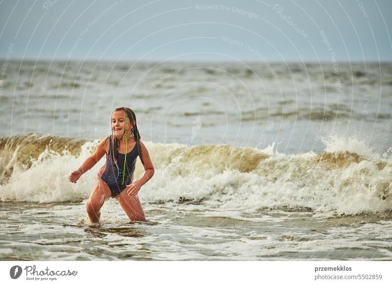 Little girl playing with waves in the sea. Kid playfully splashing in waves. Child jumping in sea. Vacations on the beach. Water splashes summer vacations ocean