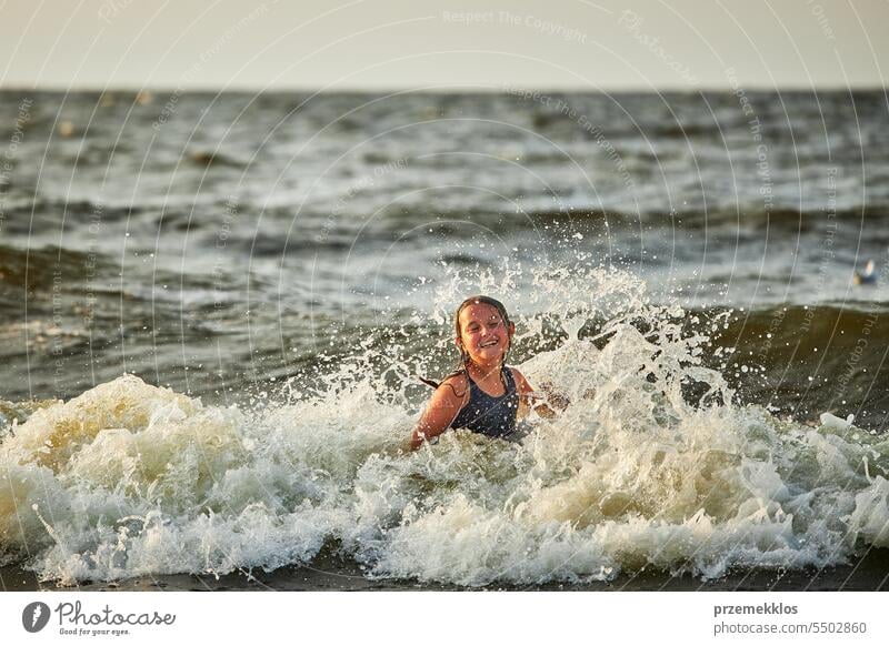 Little girl playing with waves in the sea. Kid playfully splashing with waves. Child jumping in sea waves. Summer vacation on the beach summer vacations ocean