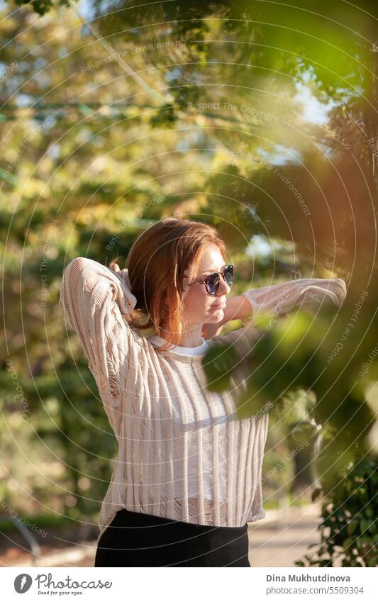 candid portrait of young beautiful woman in sunglasses backlit with sunlight in summer. Pretty ginger girl with red hair. park smiling happy pretty Smiling