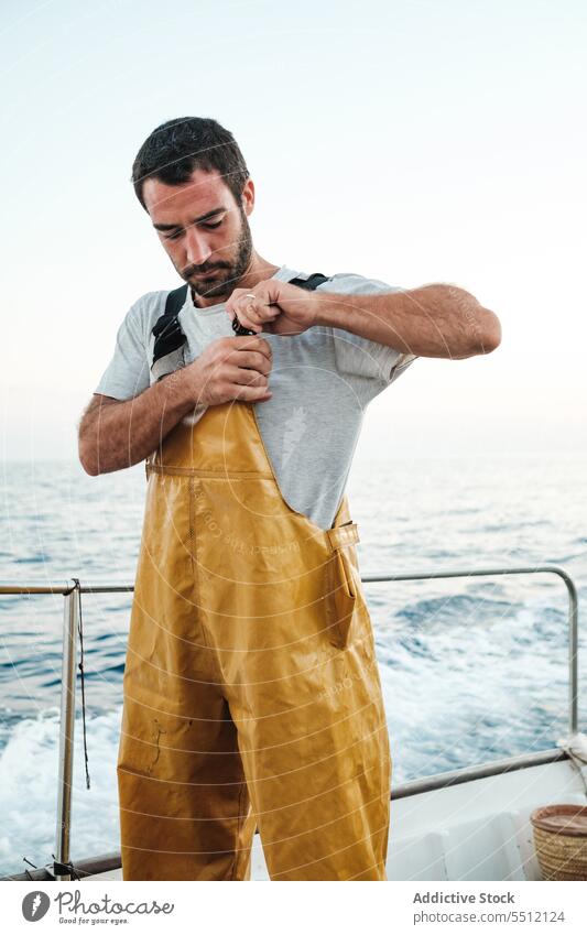 Confident young ethnic fisherman tightening braces of bib on sailboat - a  Royalty Free Stock Photo from Photocase