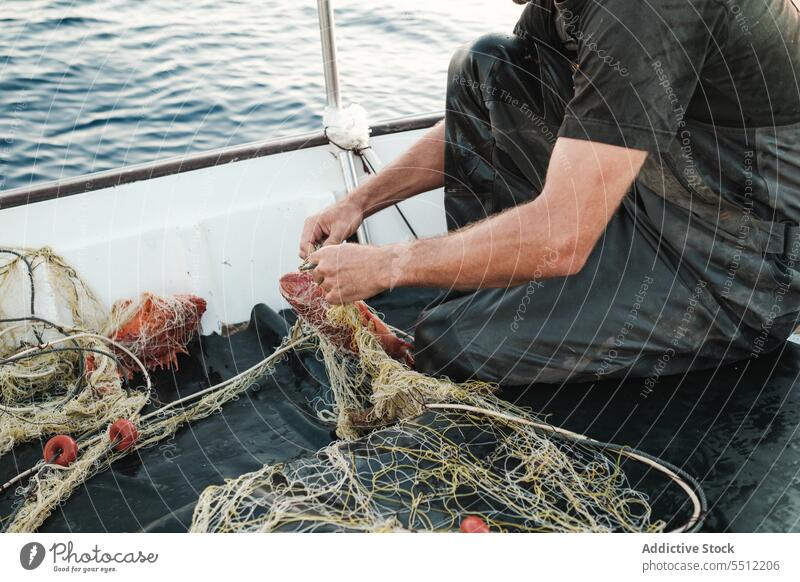 Anonymous man hand untangling fishing net threads to catch fish in