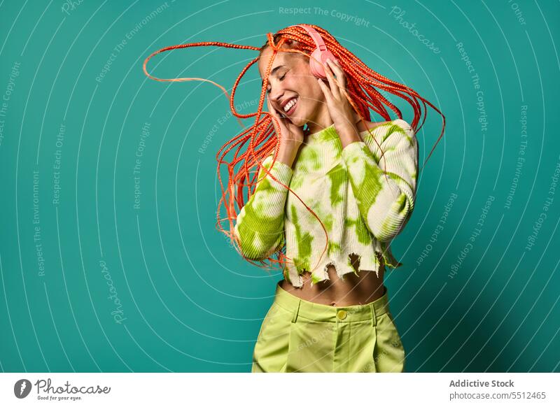 Cheerful woman with Afro braids listening to music on headphones dance vibrant jump portrait meloman stylish studio shot energy excited happy enjoy smile