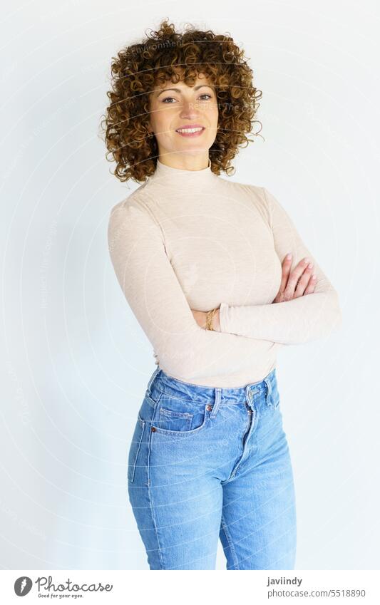 Smiling curly haired woman with hands crossed arms crossed arms folded studio shot pose portrait posture outfit smile delight confident optimist positive female
