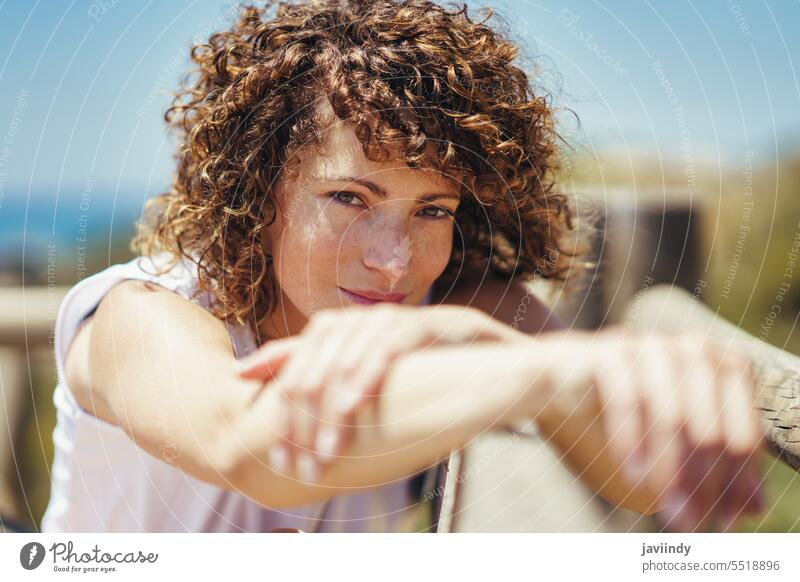 Young woman with curly hair and blurred hands lean charming urban city personality calm appearance railing peaceful relax enjoy alone lean on stare smile