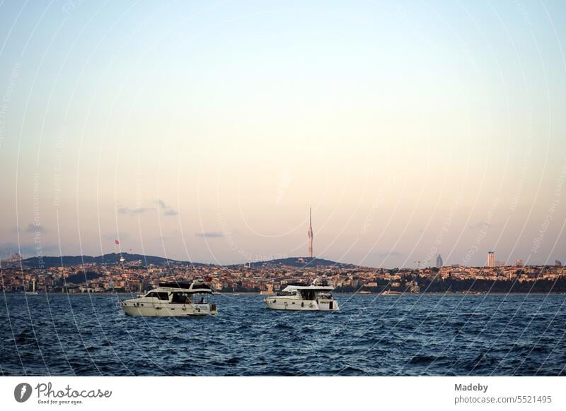 Motorboats and yachts in front of the pier of the ferry across the Bosphorus in Karaköy in the light of the setting sun with a view of the TV tower Küçük Çamlıcaim in Istanbul, Turkey