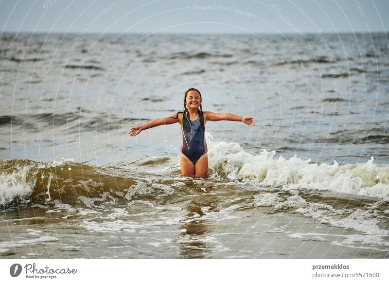 Back view of little girl in panties jumping into sea waves while having fun  on beach stock photo - OFFSET