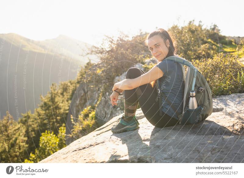 A young woman, mountaineer, rests sitting on top of a mountain, in the background the natural landscape out of focus nature traveler adventure hike backpack