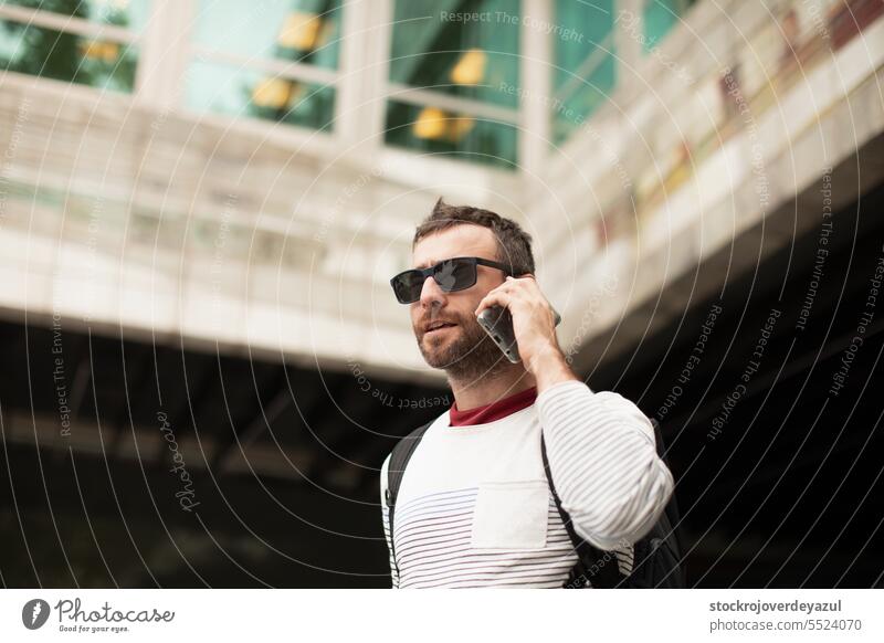 A young, traveling man wearing sunglasses, talking on a smartphone phone, on the street, in a city in Spain. men male person urban adult lifestyle outdoors