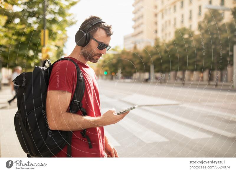 A young man wearing sunglasses, listening to music and looking at his smartphone while visiting a city in Spain. adult lifestyle male person technology street