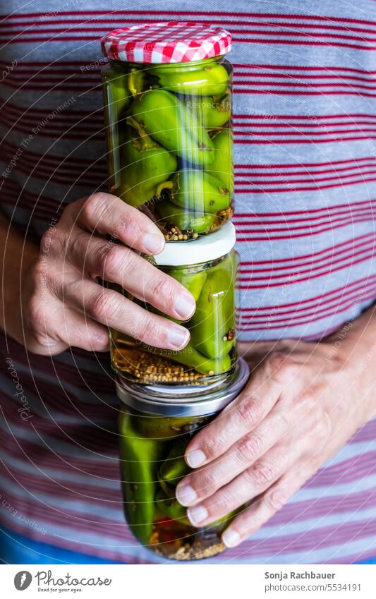 A man holds three jars of pickled green peppers in his hands Pepper Preserving jar Vinegar Canned Autumn homemade Vegetable Herbs and spices Green Conserve