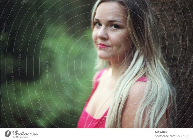 analog portrait of beautiful blonde long haired woman standing in light forest leaning against tree and looking sideways into camera Woman pretty Blonde