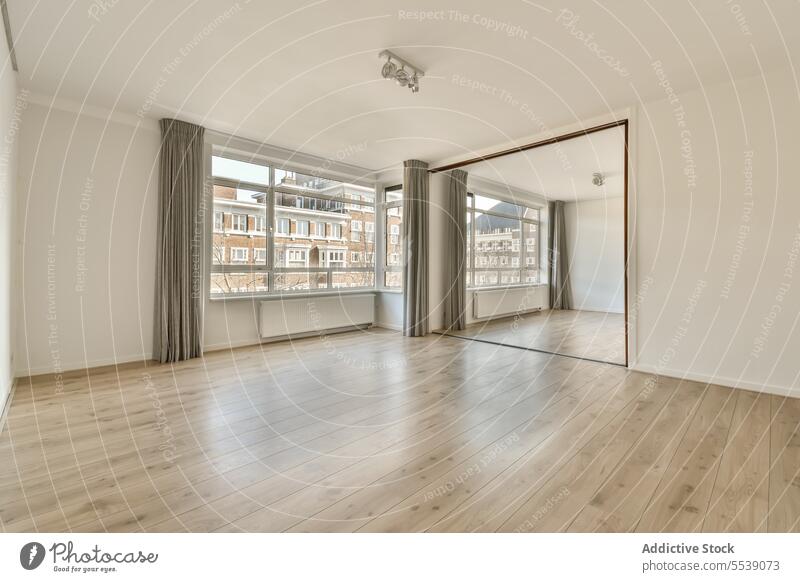 Empty living room with large window and mirror white wall house reflection unfurnished empty radiator hardwood floor curtain bright copy space daylight interior