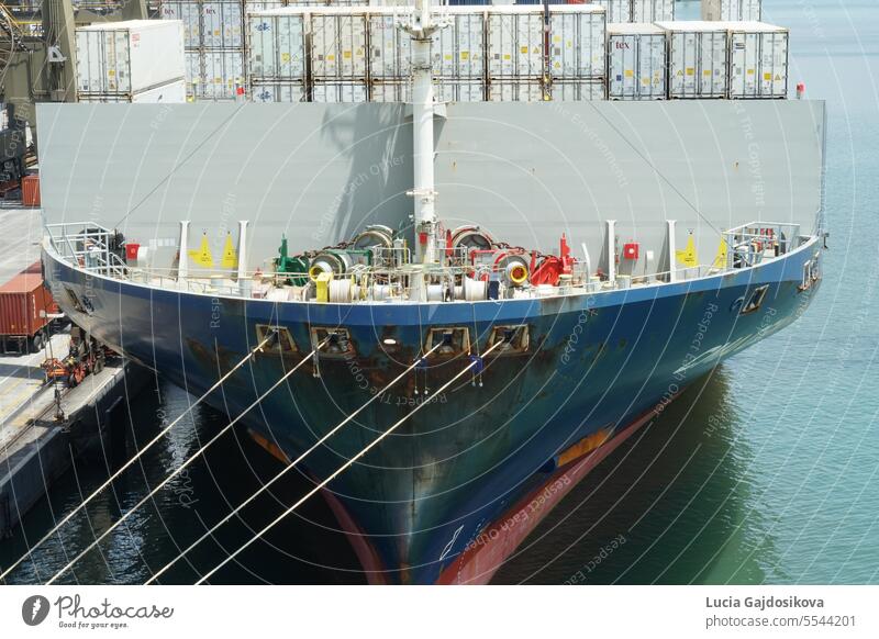 Bow and forward mooring station of the blue fully loaded vessel with reefer containers alongside in port of Kingstone under gantry cranes during cargo operation.