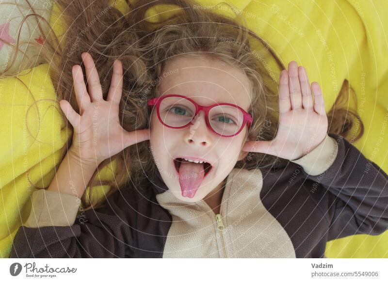 A cheerful girl in glasses makes faces, teases and shows her tongue with her hands in the form of ears, close-up. 8-10 years old Lifestyle Girl Copy space