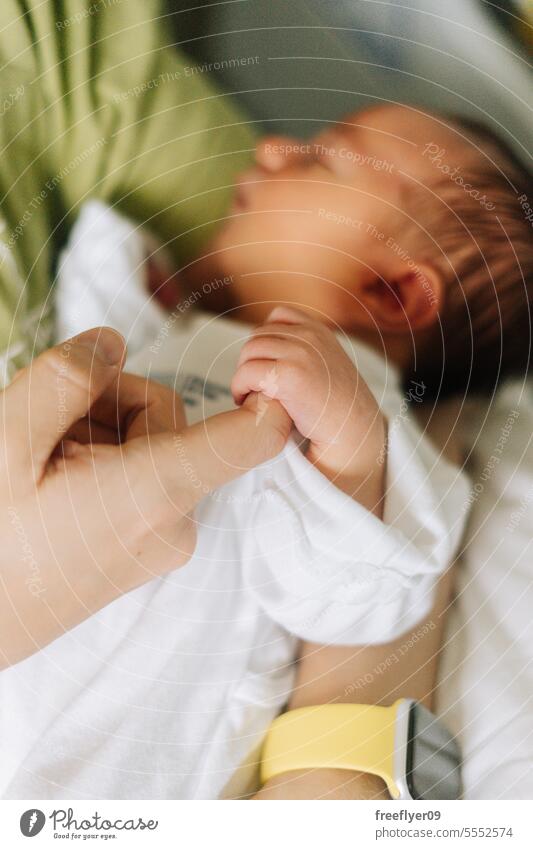 Detail of a newborn hand holding his fathers finger baby portrait care taking care copy space firstborn fatherhood parenthood mother kiss son sleeping innocence