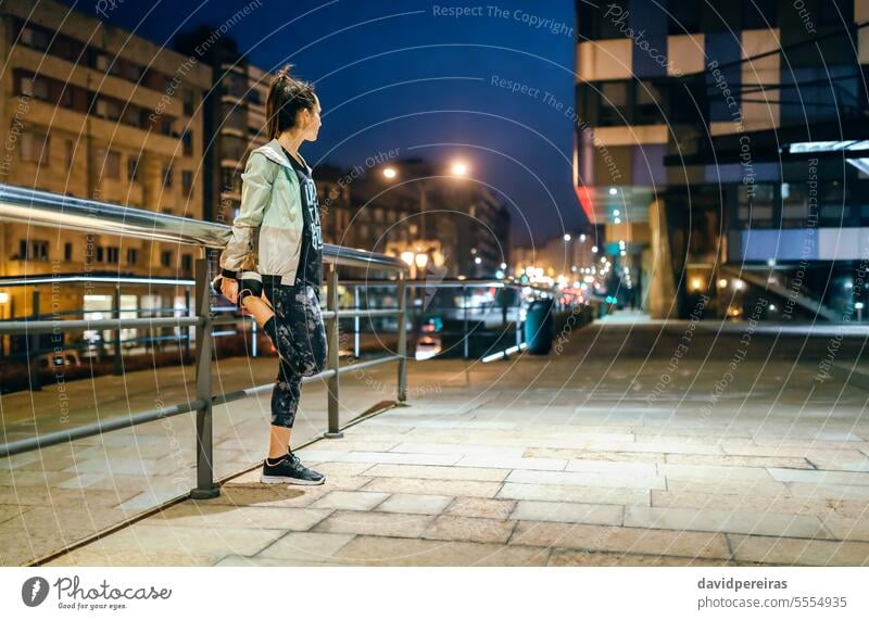 Woman runner stretching her legs next to banister before training at night on town unrecognizable female woman exercise city empty young brunette ponytail