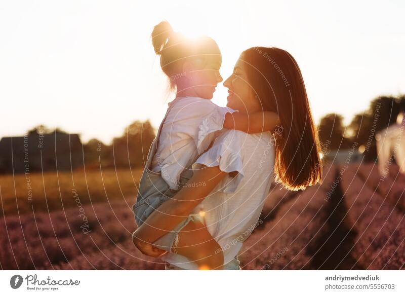 family day. young mom and little daughter enjoy relaxing in a field with lavender at sunset. A beautiful mother hugs and kiss child girl tightly. Maternal care and love for the child. mothers day