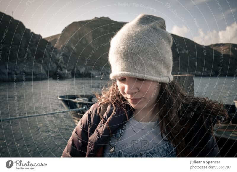 Teenage girl wearing beanie looking down to the ground, seascape young female ocean cliffs young girl