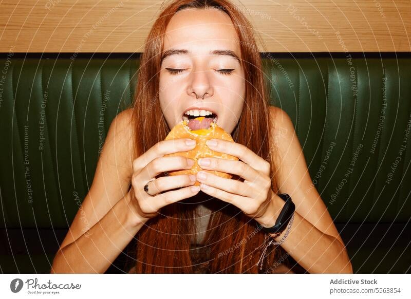 Young woman enjoy eating hamburger girl fast food young table sitting one dinner lunch snack holding hand unhealthy nutrition indoors restaurant redhead