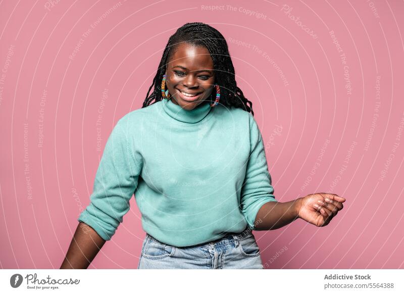 Joyful African woman laughing in teal sweater african pink background joyful happiness emotion genuine smile teeth braid hairstyle colorful earrings accessory
