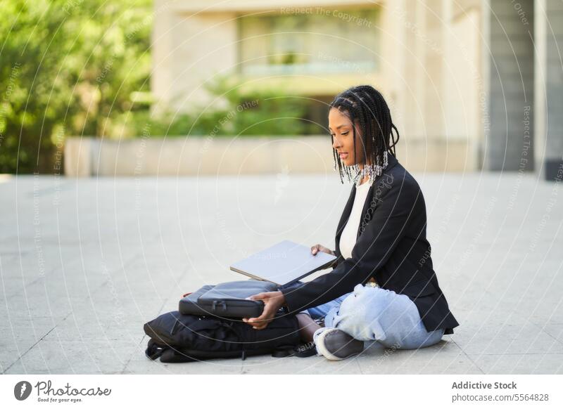 African American woman sitting on floor with laptop against blurred background of building street businesswoman modern work netbook entrepreneur casual using