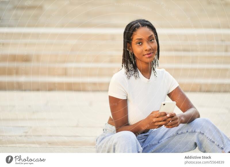 Young ethnic woman browsing mobile phone while sitting on stairs smartphone using staircase happy surfing smile step stairway connection cellphone positive